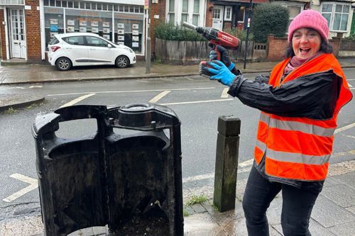 Judi wearing a high vis jacket holding a drill above an old broken bin